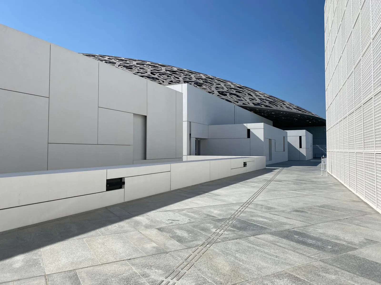 The perforated dome and white geometric buildings of Louvre Abu Dhabi under a blue sky