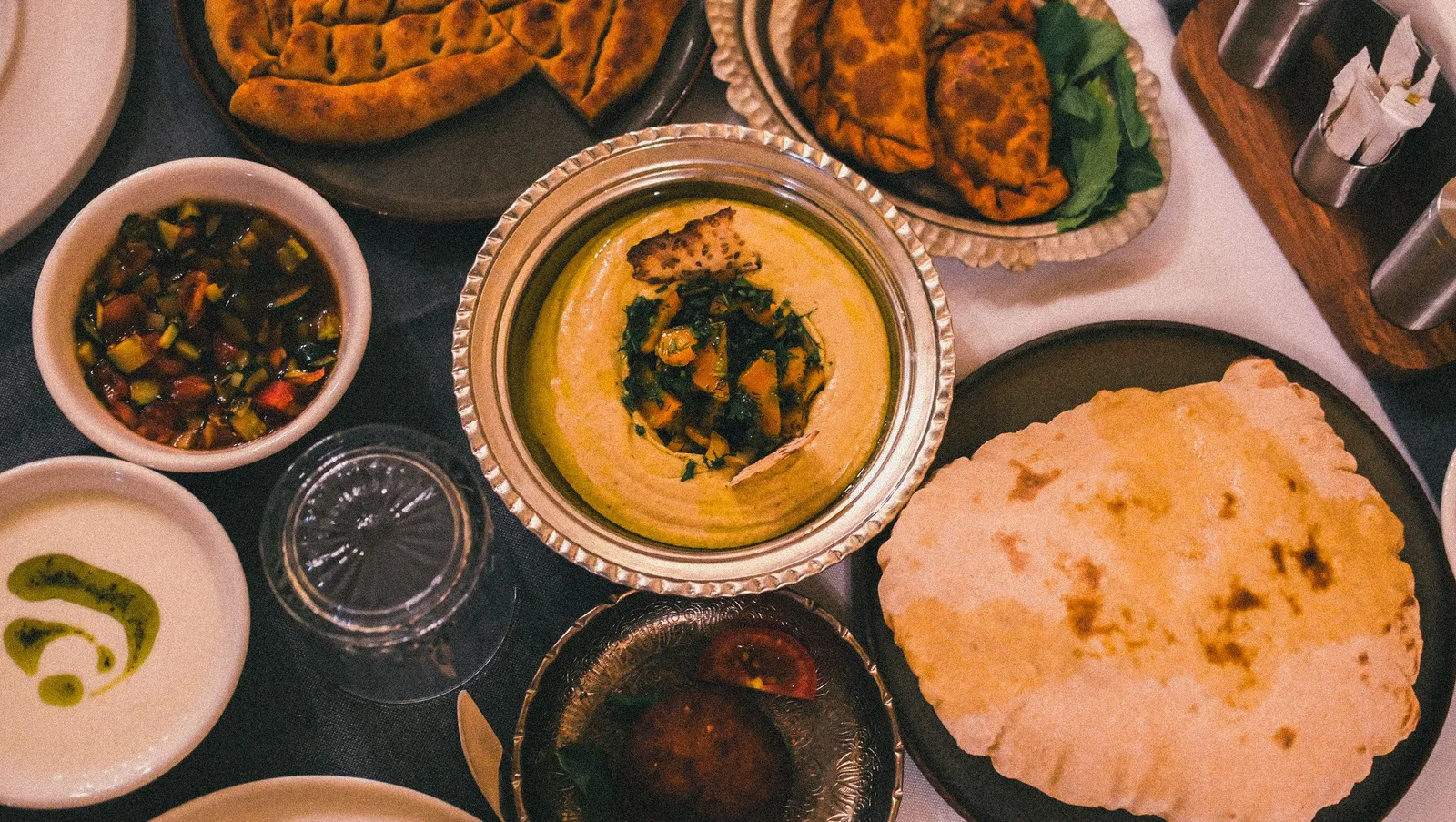 An overhead spread of Middle Eastern mezze with hummus, flatbreads, salads and pastries on a restaurant table