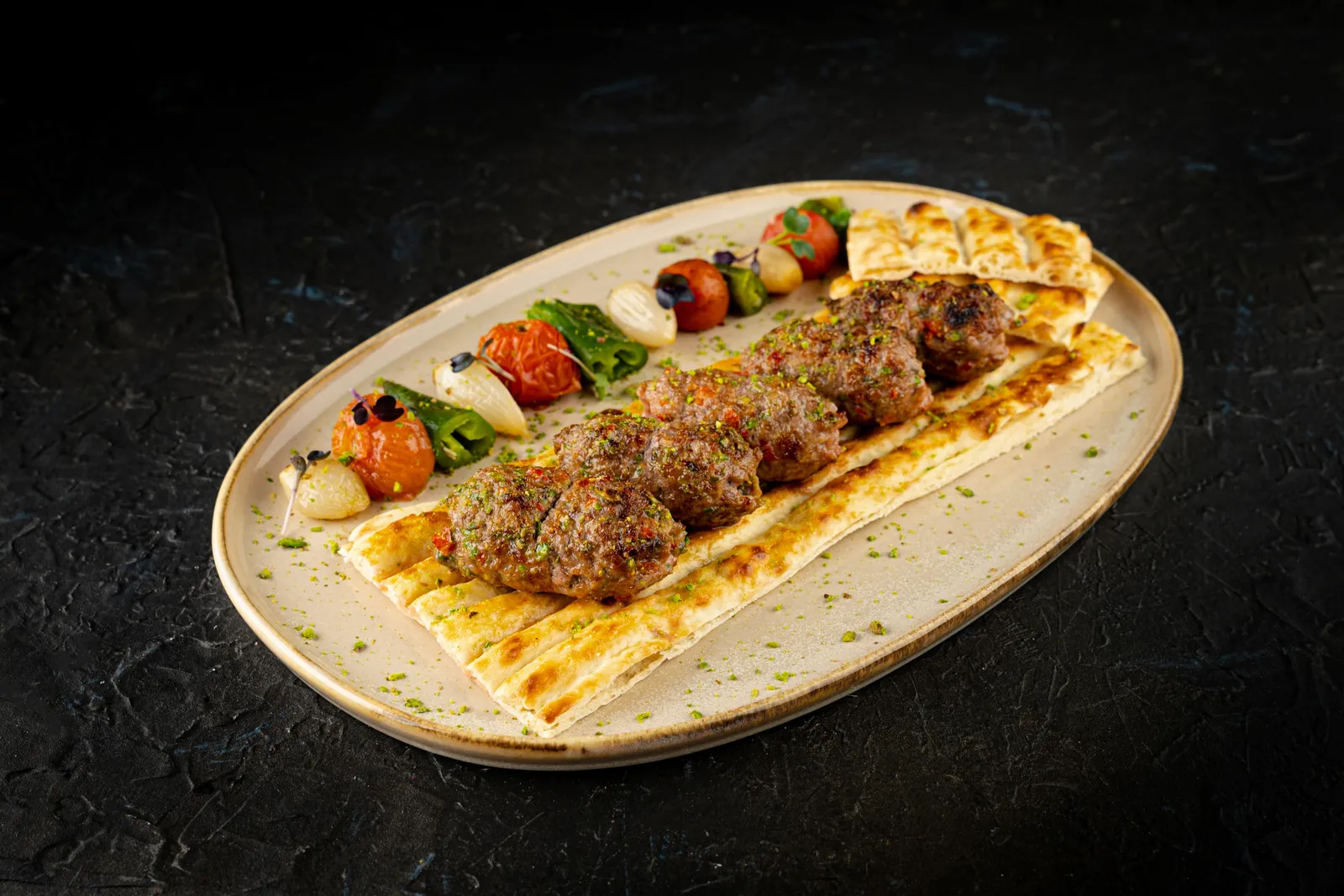 A plate of grilled kofta with flatbread and charred vegetables