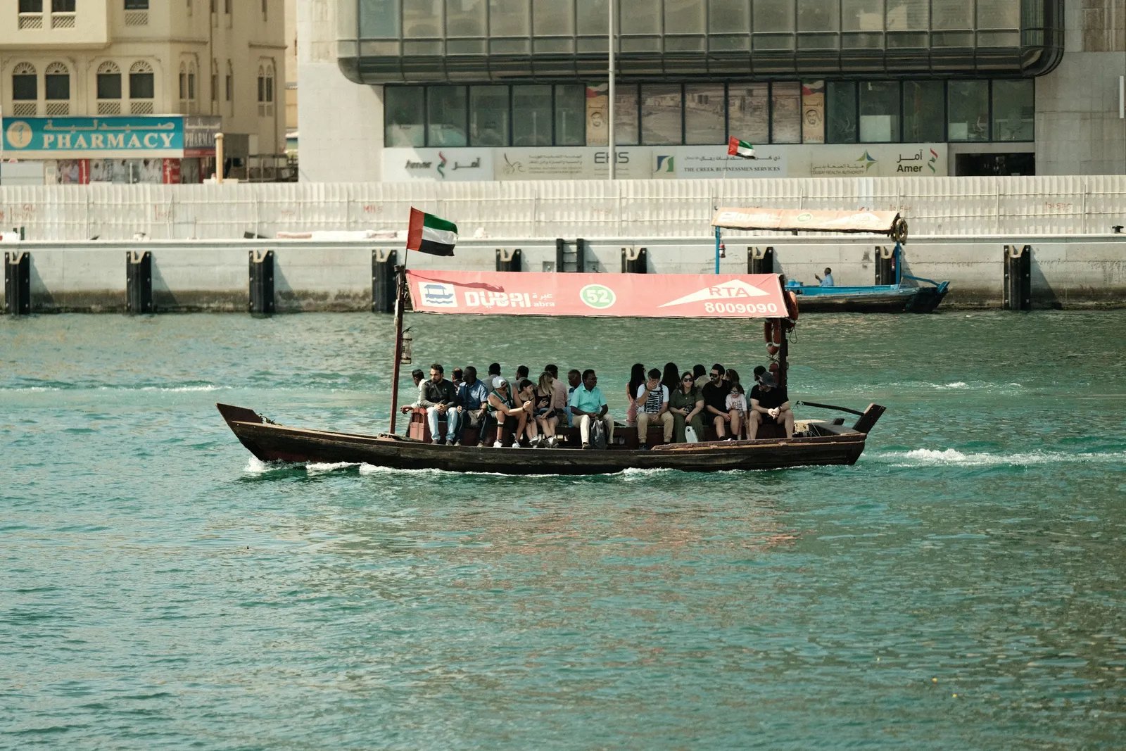 Passengers seated on the wooden bench of an abra crossing Dubai Creek with the Deira waterfront behind