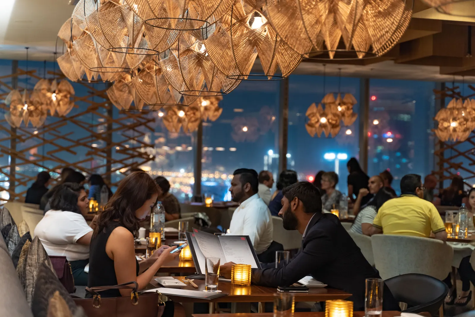 The lit interior of a licensed restaurant in Dubai at night, with diners at tables and the city visible through the windows