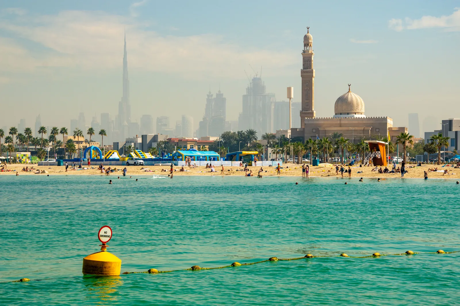 A public beach in Dubai with the city skyline behind and people swimming, United Arab Emirates
