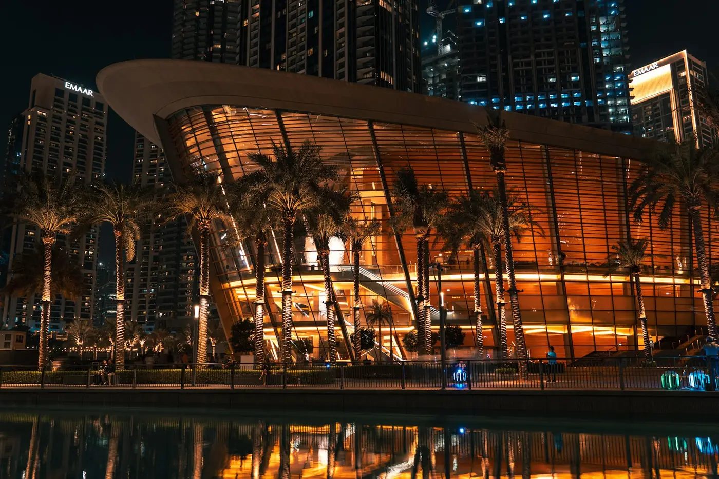 Dubai Opera's glass and steel dhow shaped facade lit up at night and reflected in the water in front of it