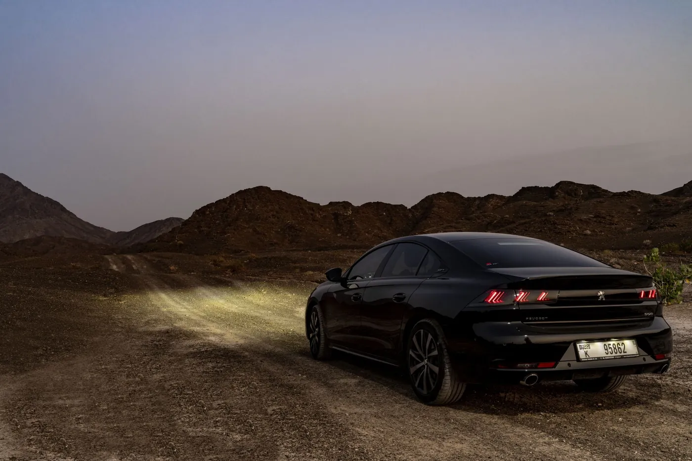 A car parked on a desert track outside Dubai with hills rising in the distance at dusk