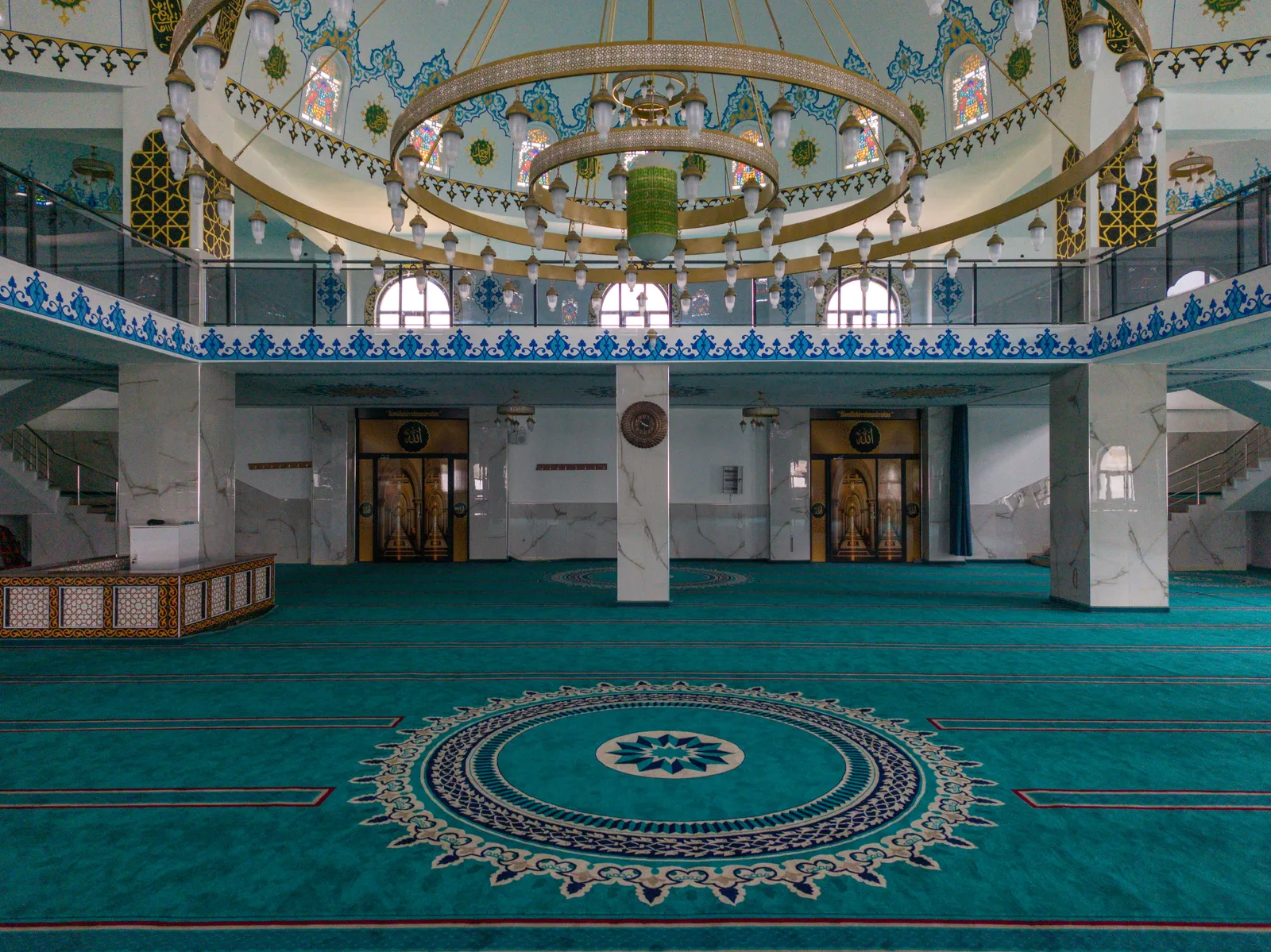 A mosque prayer hall with patterned carpet, arches and hanging lamps