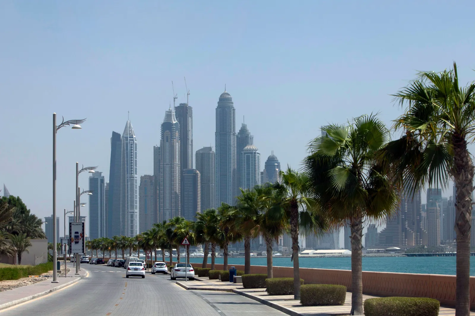 A palm-lined coastal road in Dubai with high-rise towers behind
