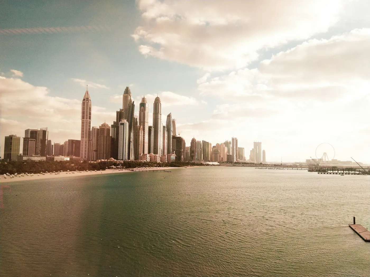 The long beachfront promenade at JBR in Dubai with high rise towers behind the sand and sea in the foreground