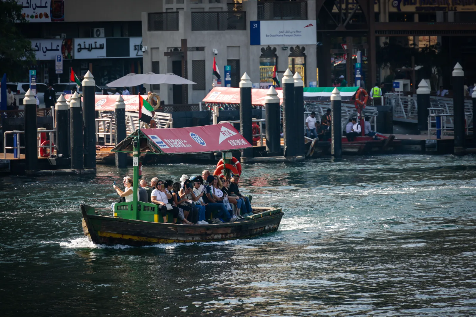 A traditional wooden abra boat carrying passengers across Dubai Creek in daylight