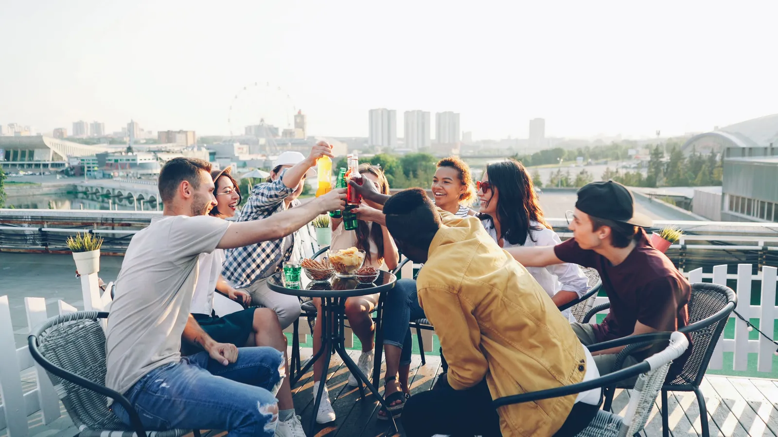 People toasting drinks at an outdoor terrace table with a city skyline behind them
