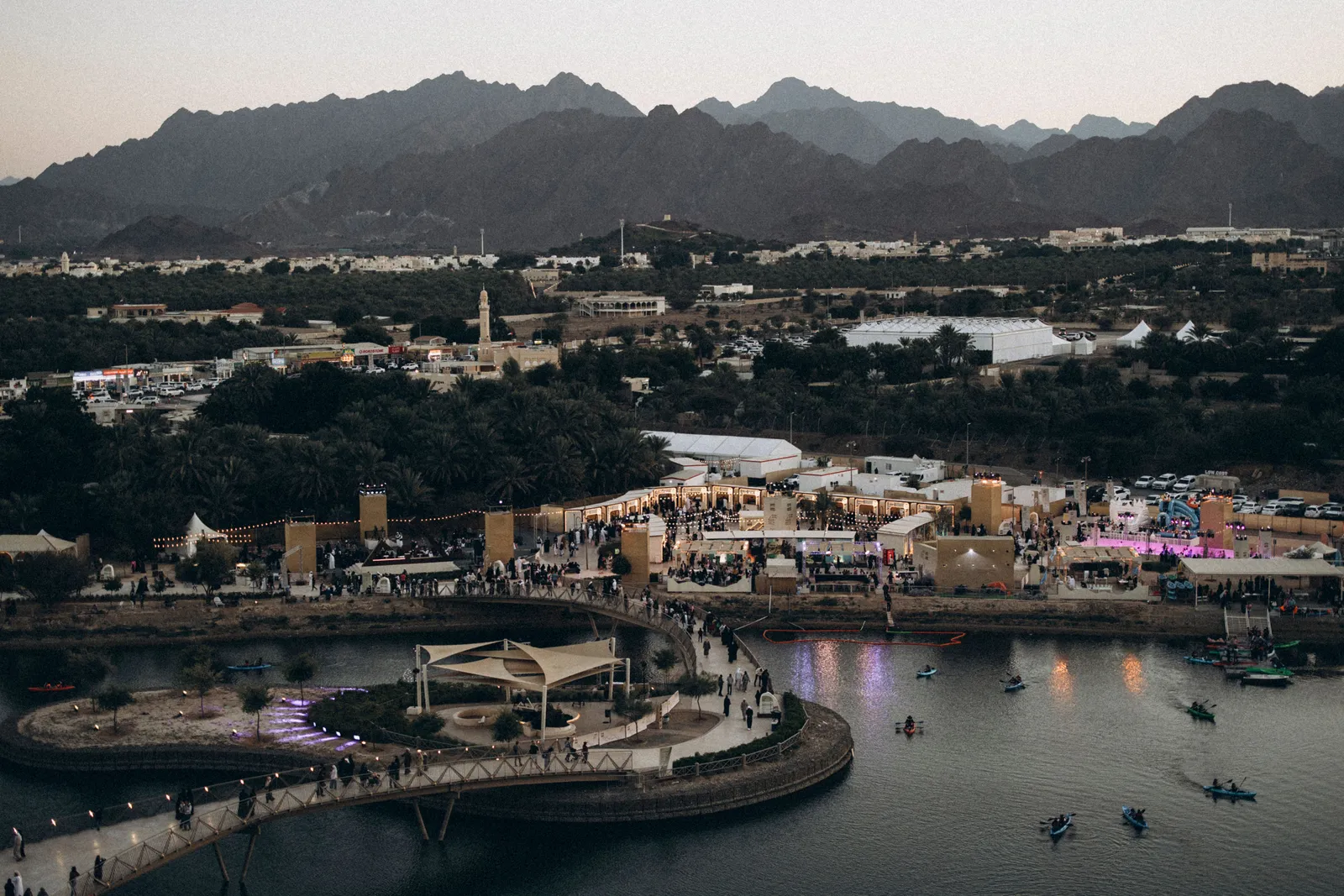 Aerial view of Hatta at dusk with the lake, the illuminated waterfront and the Hajar mountains behind