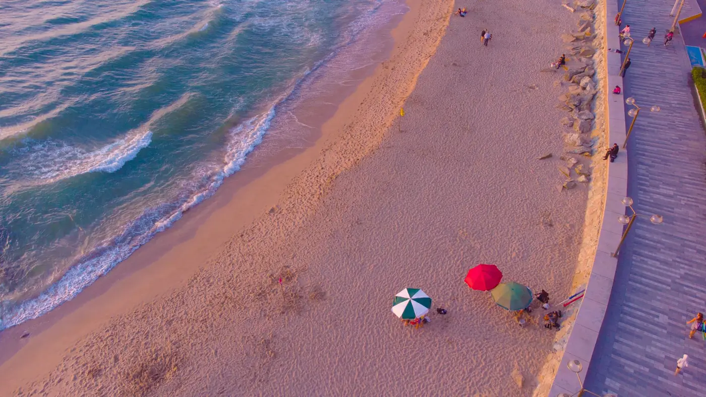 An aerial view of a sandy beach and promenade with colourful sun umbrellas at twilight