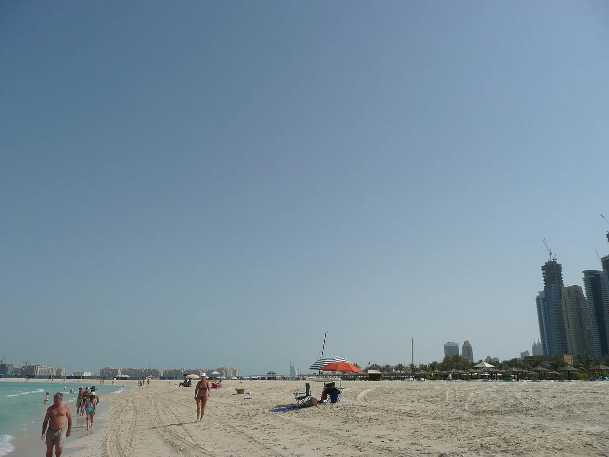 A wide shallow sand beach, with pale towers on the hazy horizon