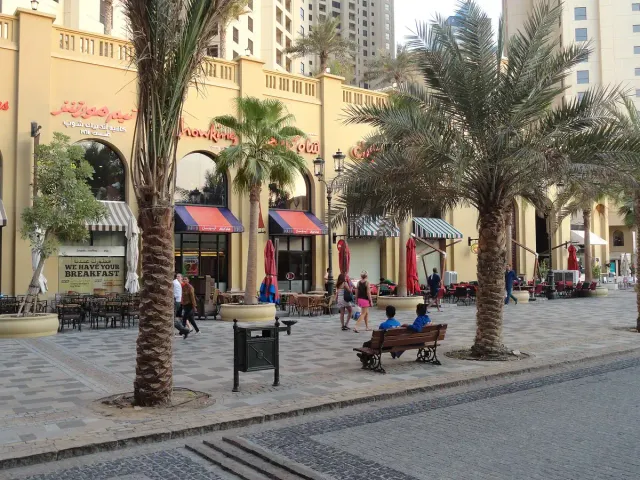 A wide paved promenade lined with tall palms, benches and cafes on both sides