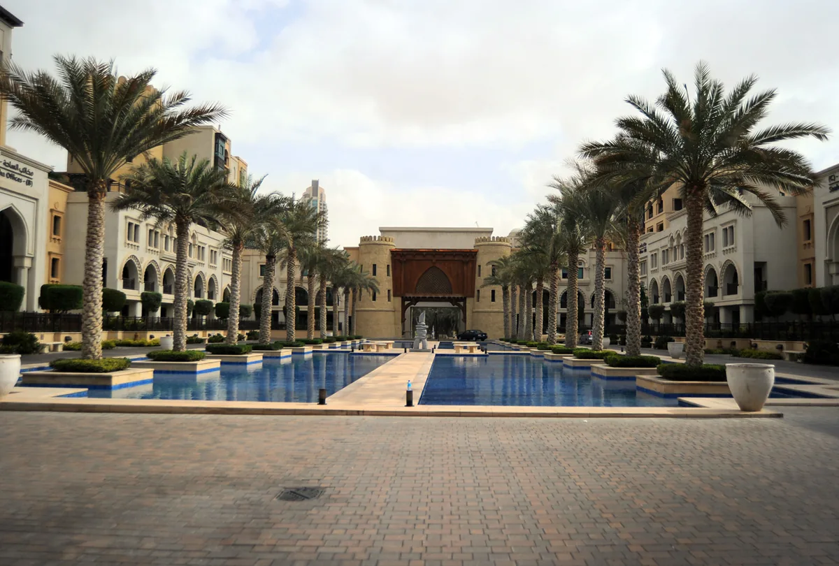 A plaza with a long water channel and palms
