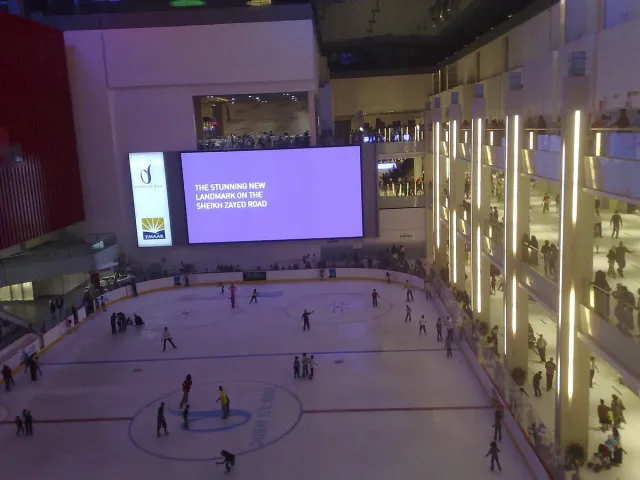 An indoor ice rink inside a mall with skaters and viewing balconies around it