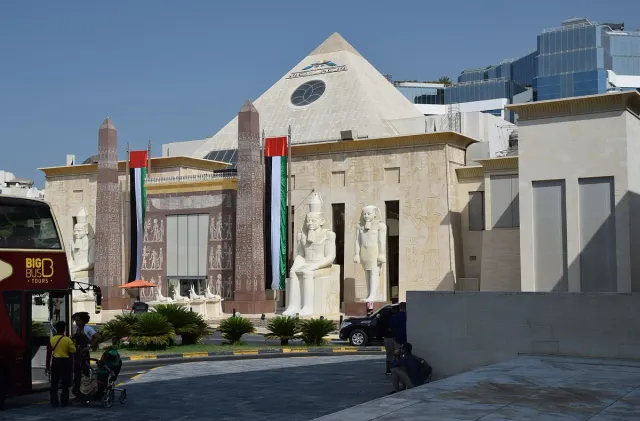 An ancient Egyptian style facade with large statues, columns and flags beside a triangular roof