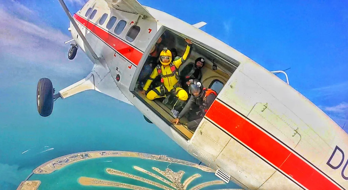 A skydiver in a yellow suit in an open aircraft door above the palm island