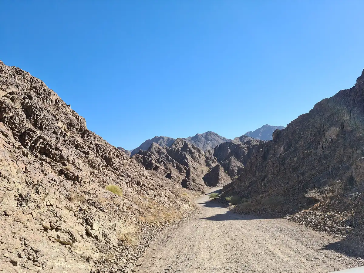 A dirt track winding between bare rocky ridges under a clear sky