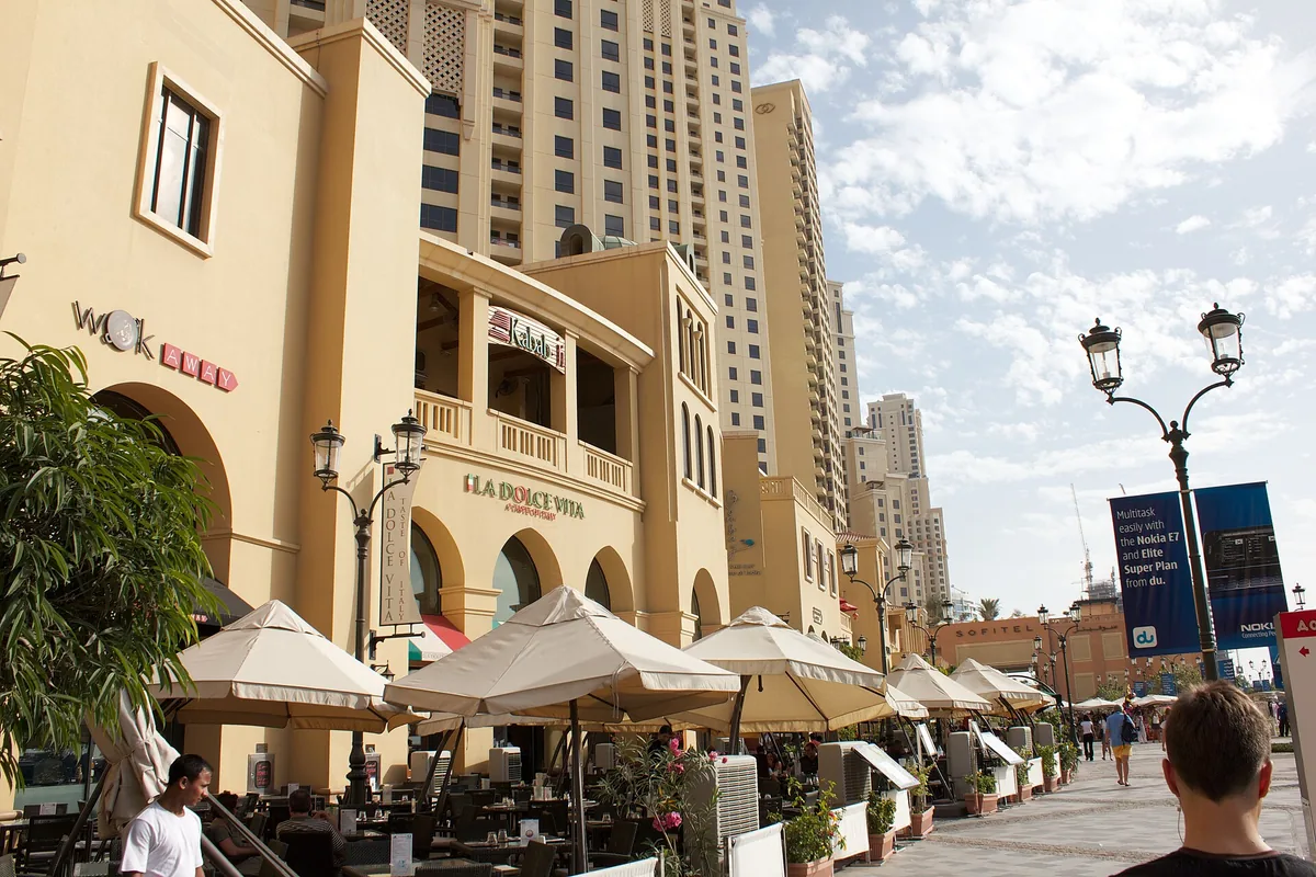 A promenade of restaurants with parasols and palms