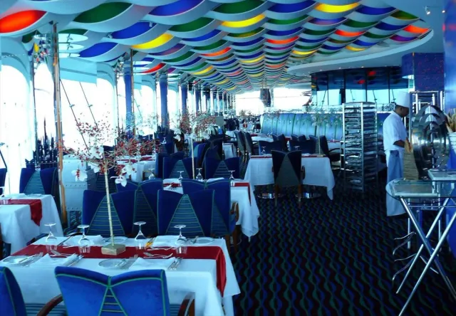 A restaurant hall with tables set in white under a wavy ceiling in bold colour stripes