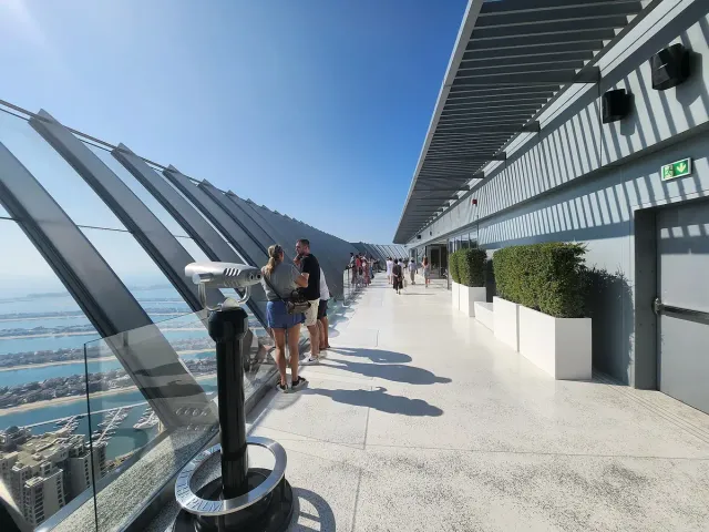 An open observation terrace with viewing binoculars, a glass railing and the sea below