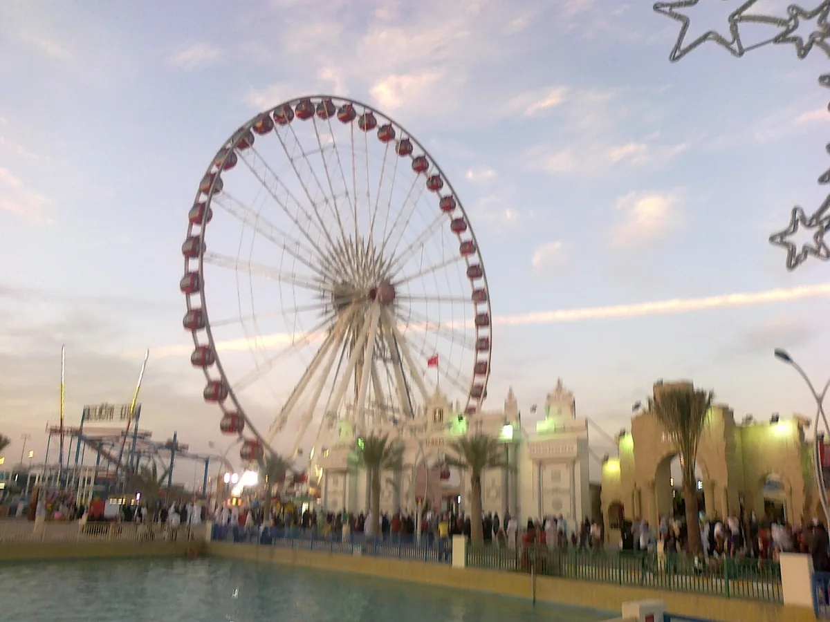 An illuminated ferris wheel above festival pavilions and a crowd of visitors