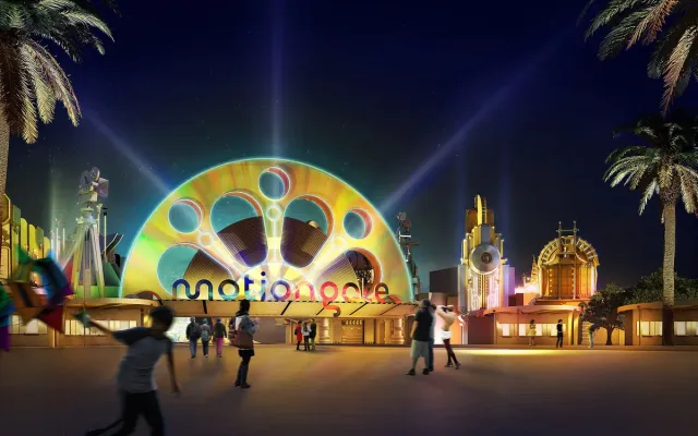 An illuminated film reel shaped entrance arch with beams of light in the night sky