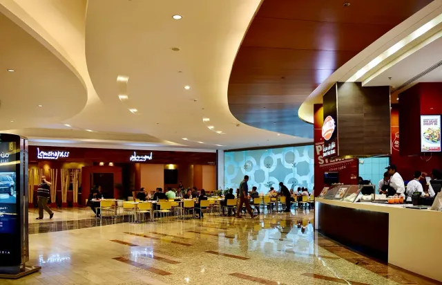 A mall dining hall with lit counters, tables and yellow chairs