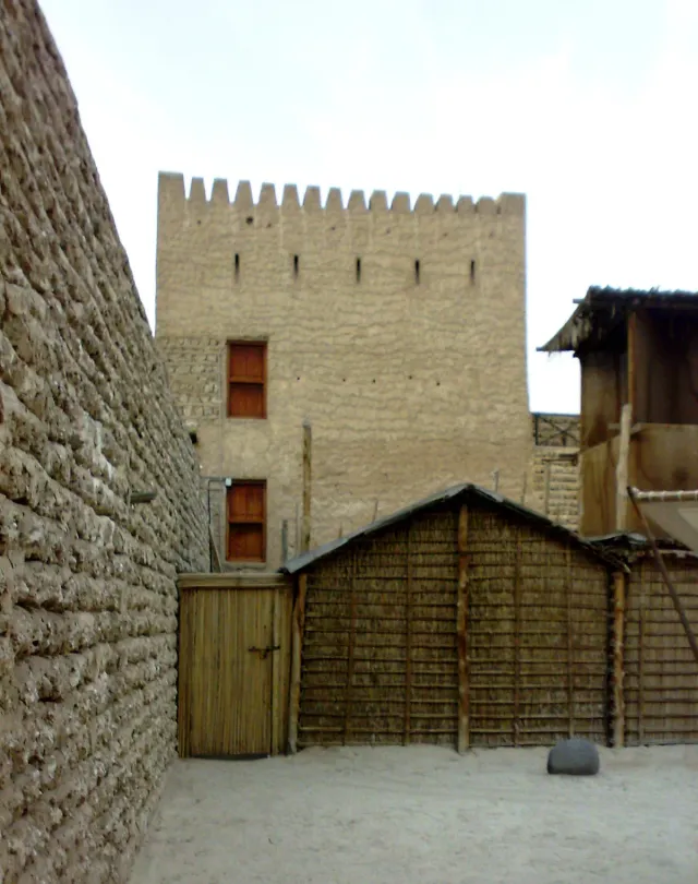 The coral stone wall of a fort with a tower and shelters made of palm branches