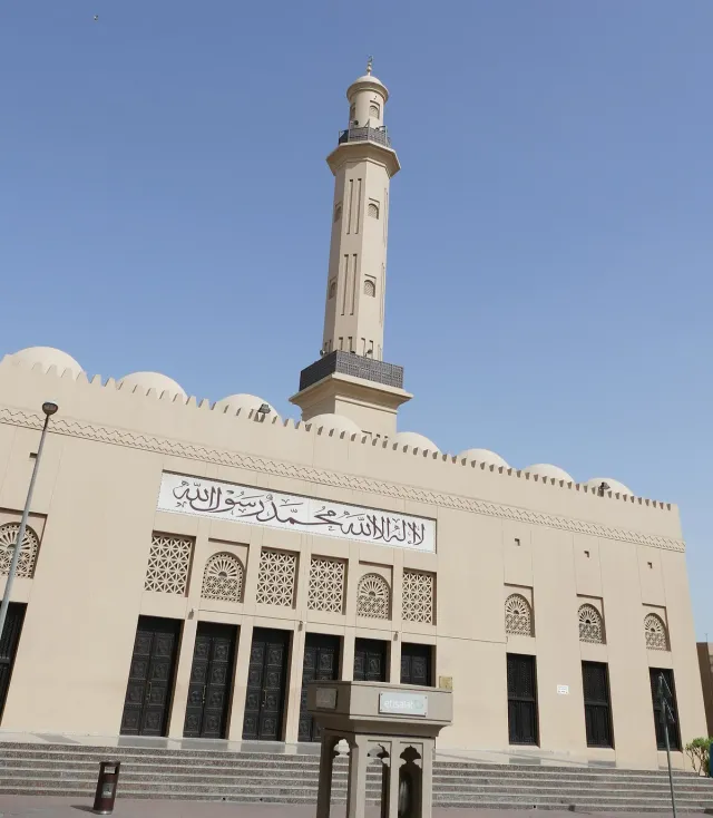 A white mosque with a tall minaret and carved script above a row of arches