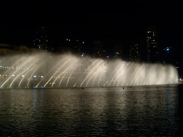 Lit water jets rising above a lake in the evening