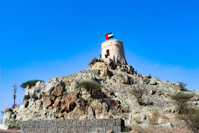 A round stone watchtower on top of a rocky hill under a blue sky