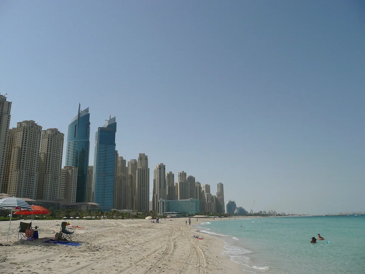 A quiet beach with blue water and a line of towers at the far end
