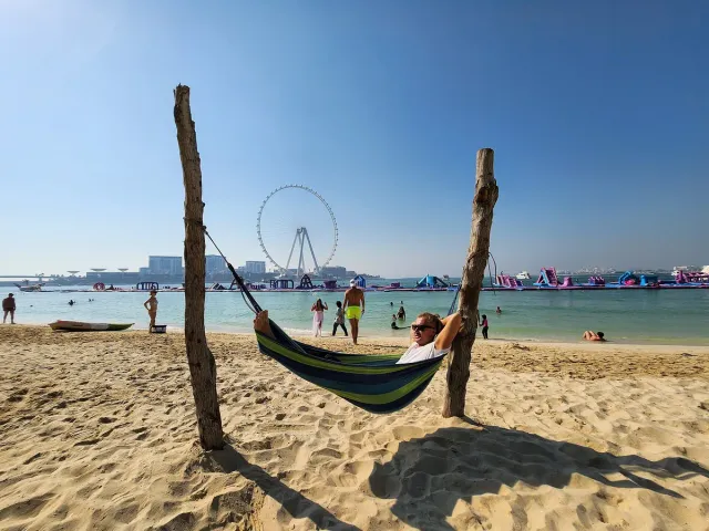 A colourful hammock between two posts on white sand with a giant wheel behind