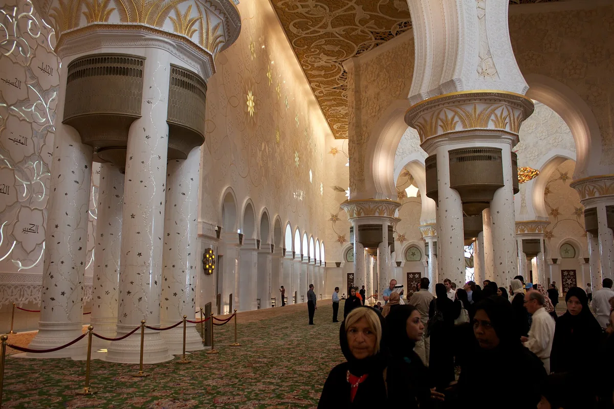A prayer hall with decorated columns and visitors
