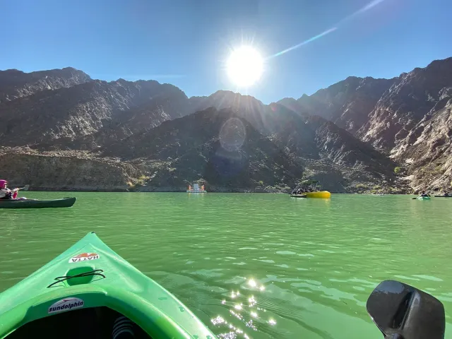 A green kayak on greenish lake water between bare mountains under a low sun