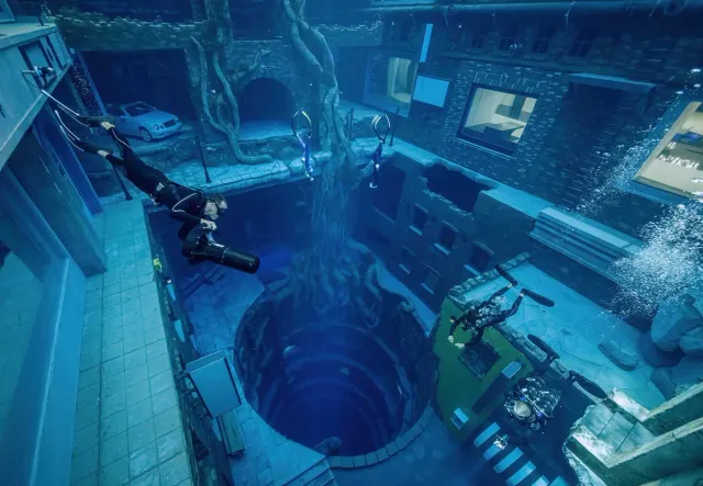 A deep dive pool with a lit sunken city set and a diver descending from above
