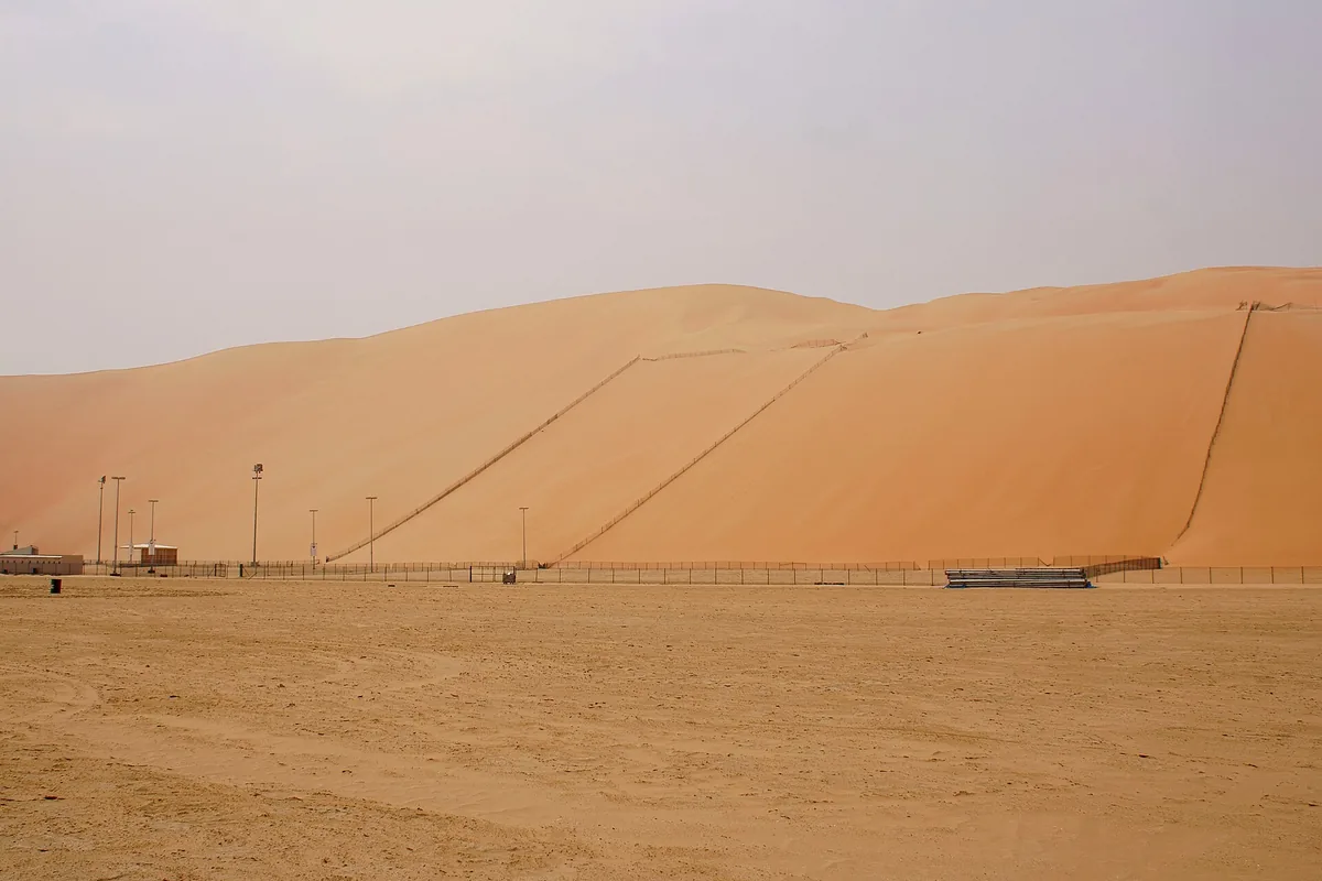 A vast reddish sand dune rising above a flat plain under a hazy sky