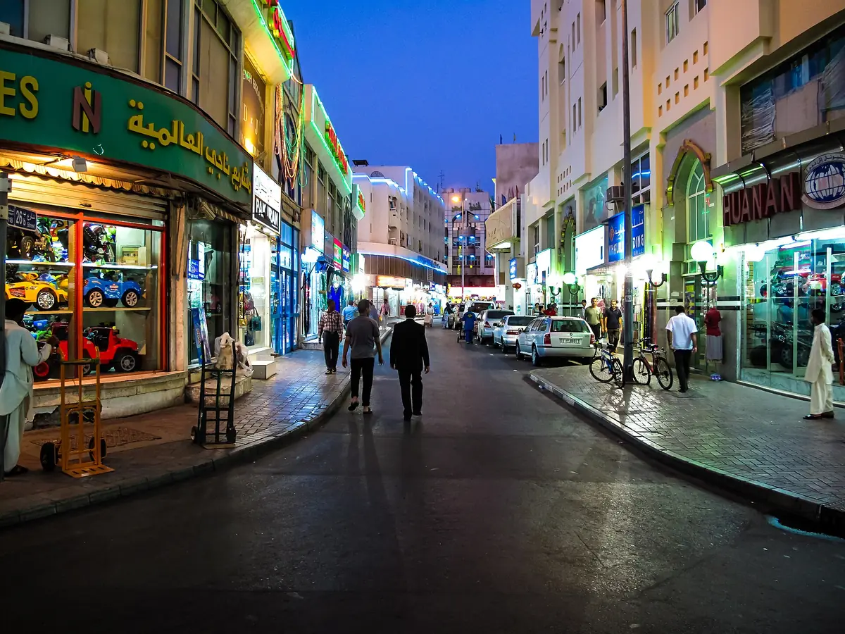 A shop lined street lit by signs in the evening