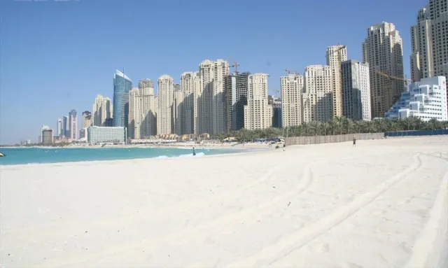 A wide strip of white sand facing turquoise water and a wall of residential towers