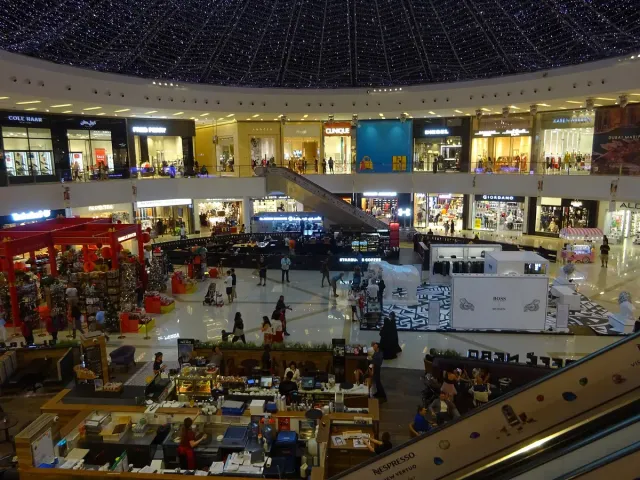 A multi level mall atrium with lit stores and visitors moving through