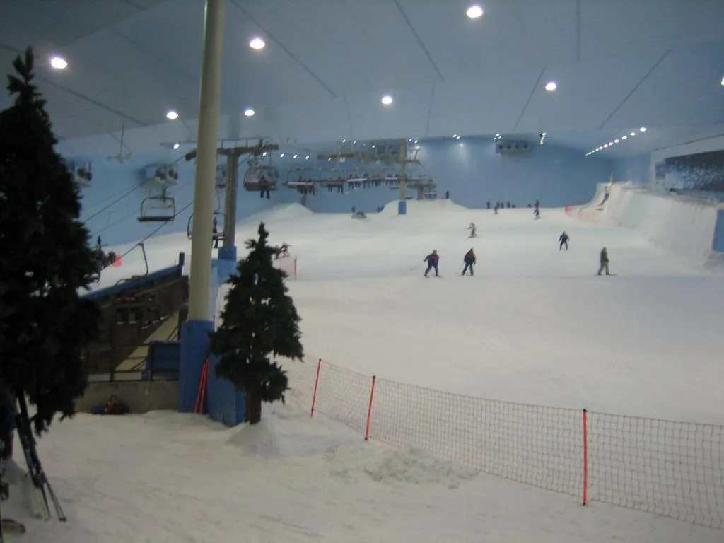 A snow covered ski slope inside a covered hall with a chairlift and skiers