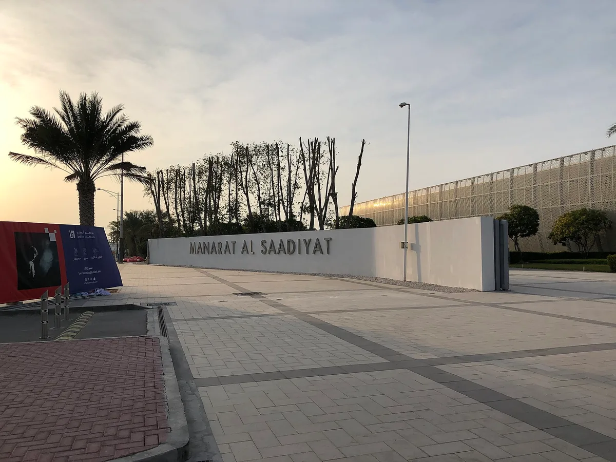 The entrance wall carrying the name Manarat Al Saadiyat, with the perforated metal facade of the arts centre behind it at dusk