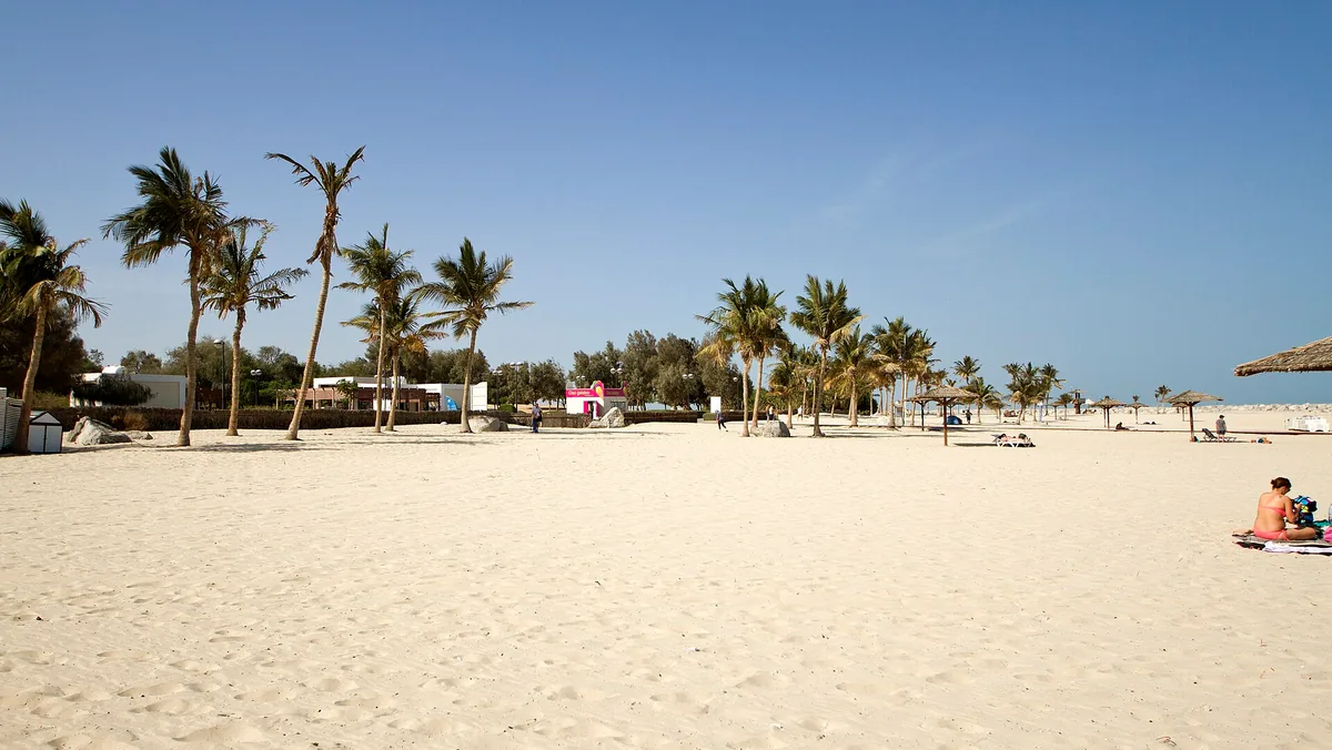 A palm grove and shade huts on pale sand under a blue sky