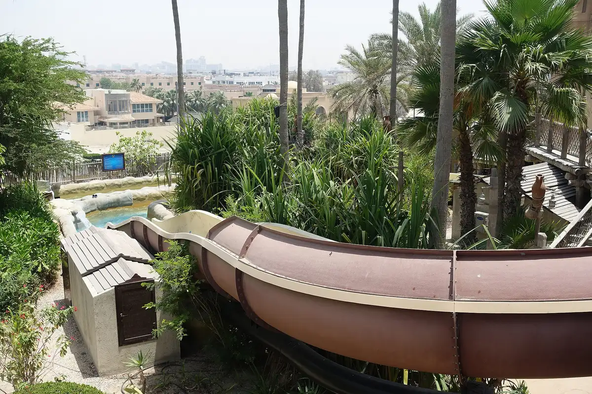 A winding water slide curving between palms above a pool