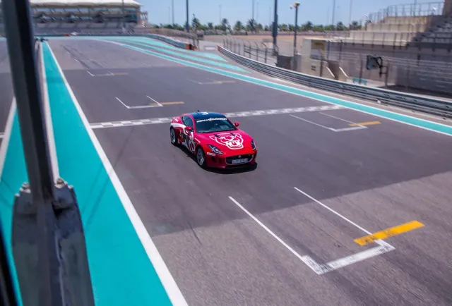 A red race car on an asphalt track with turquoise run off areas and grandstands