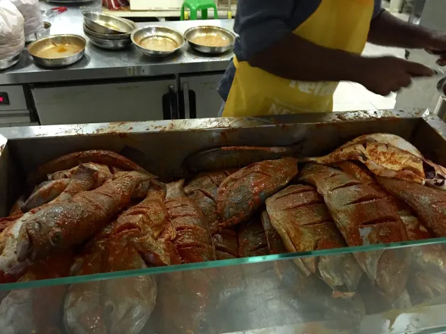 A tray of whole fish coated in red spice mix behind a glass counter