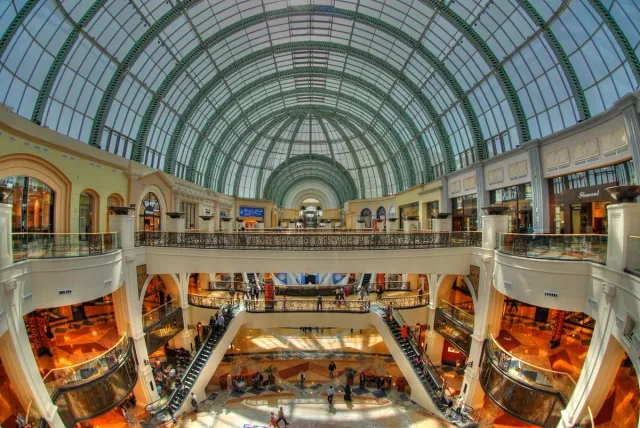 A large mall atrium with an arched glass roof and stores on several levels