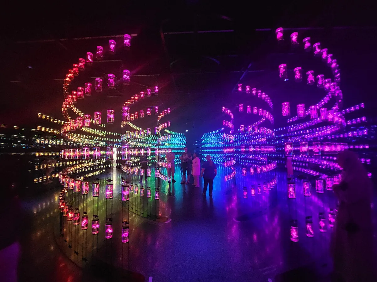 A corridor of glowing pink and blue jars reflected in the floor