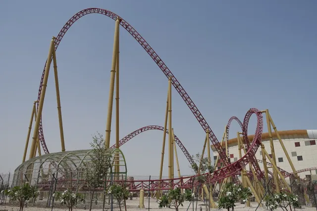 A tall roller coaster with loops rising beside the park building